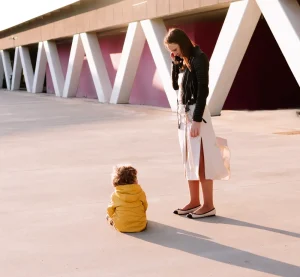 Distracted parent on the phone while a toddler sits on the ground during a temper tantrum in a public outing