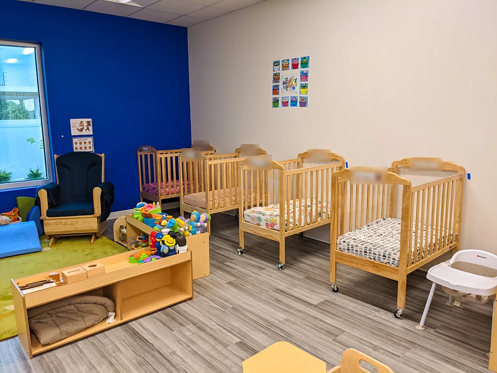 Amazing Explorers Academy infant classroom with wooden cribs, a rocking chair, and toy shelves